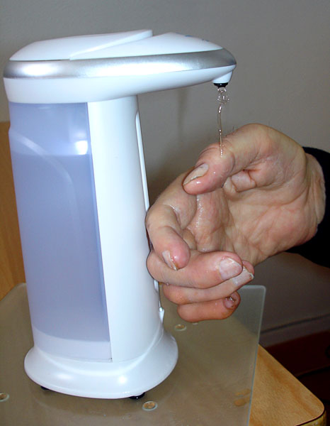 Användaren håller handen under pumpen av den automatiska tvålautomat. Handsprit rinner på användarens hand. 